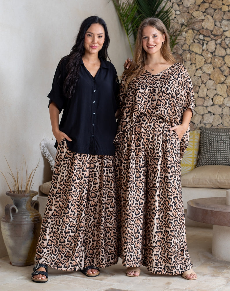 Two women wearing leopard print dresses standing in a room with a stone wall and decorative elements.