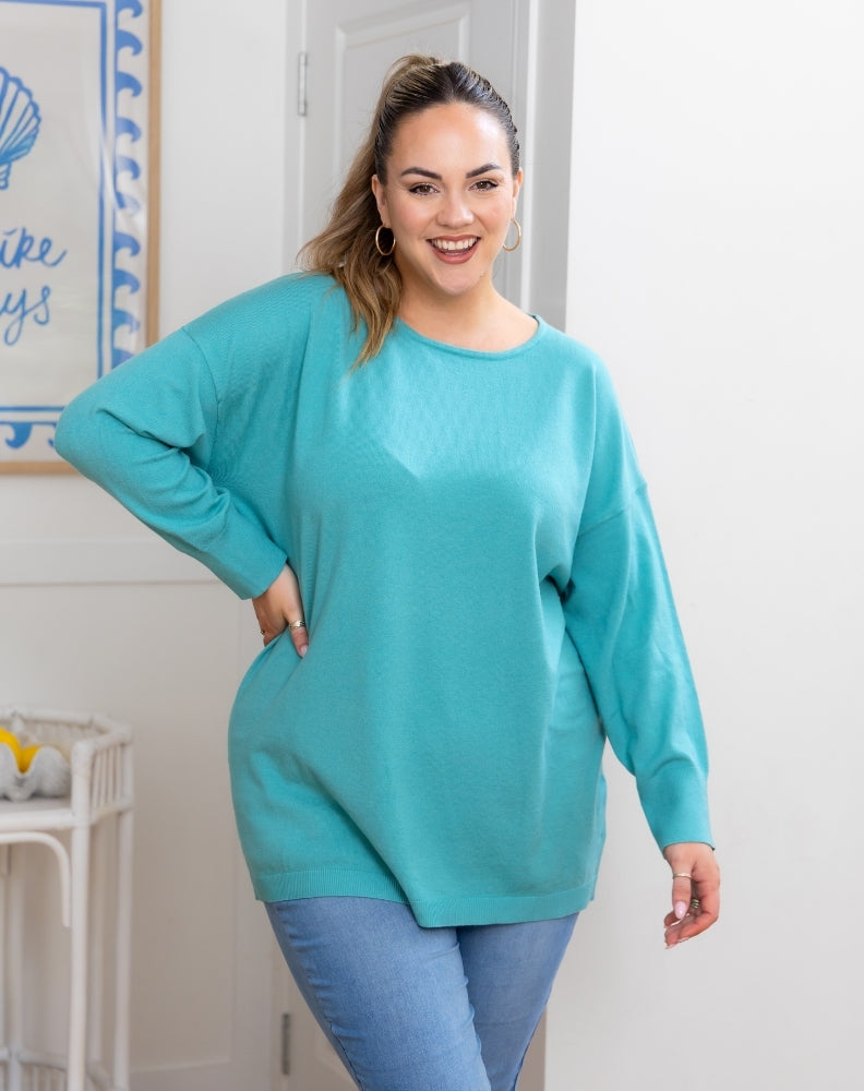 Woman wearing a teal sweater and blue jeans indoors.