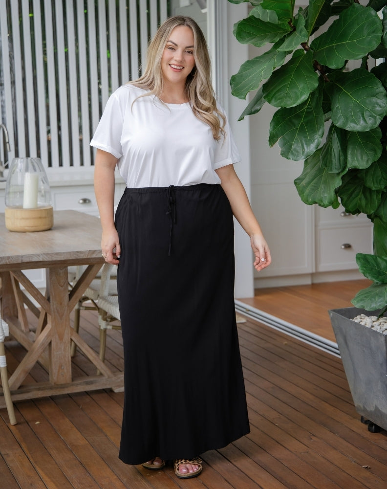 Woman wearing a white top and black skirt standing on a wooden deck.
