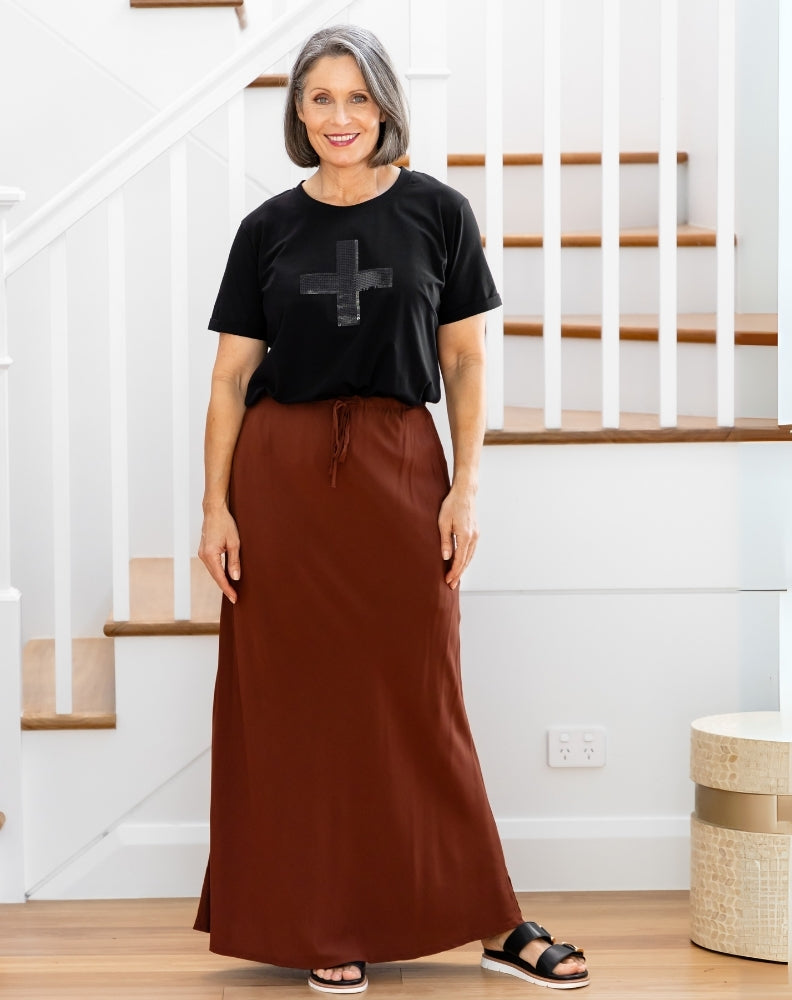 Woman wearing a black t-shirt with a graphic design and a brown skirt indoors.