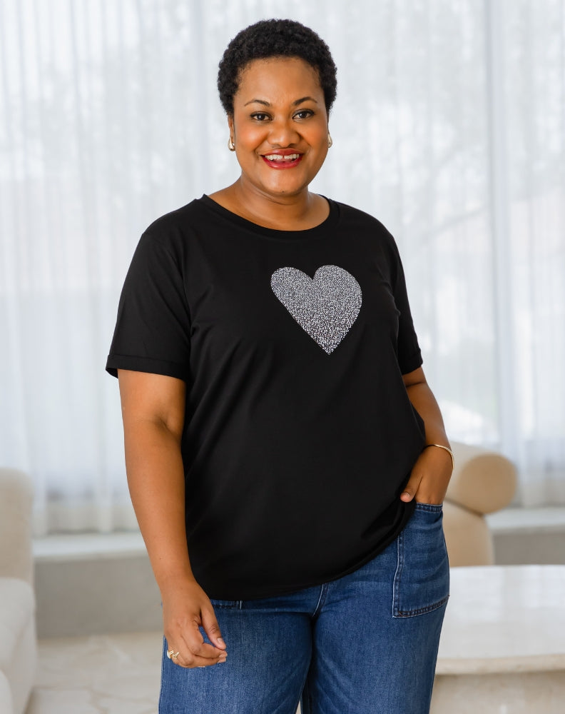 Woman wearing a black t-shirt with a silver heart design in a living room.