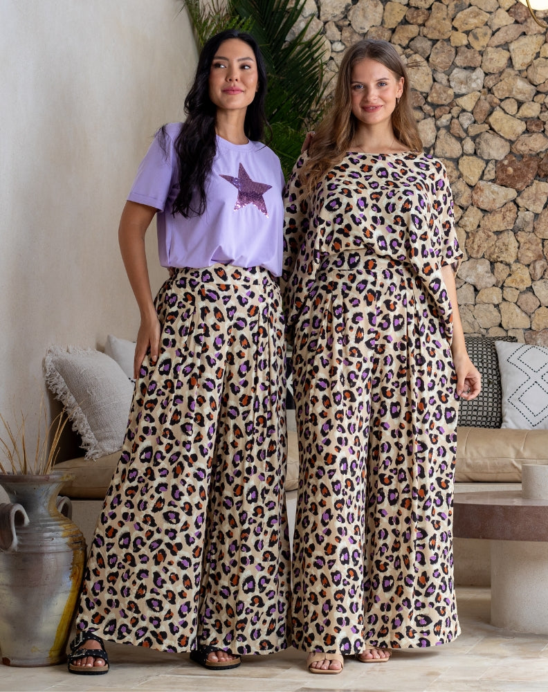 Two women wearing leopard print outfits standing in a room with a stone wall and plants.