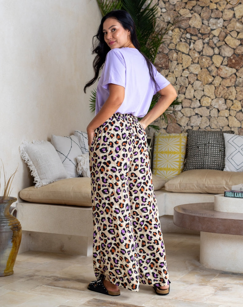 Woman wearing a light purple shirt and leopard print pants standing in a living room.