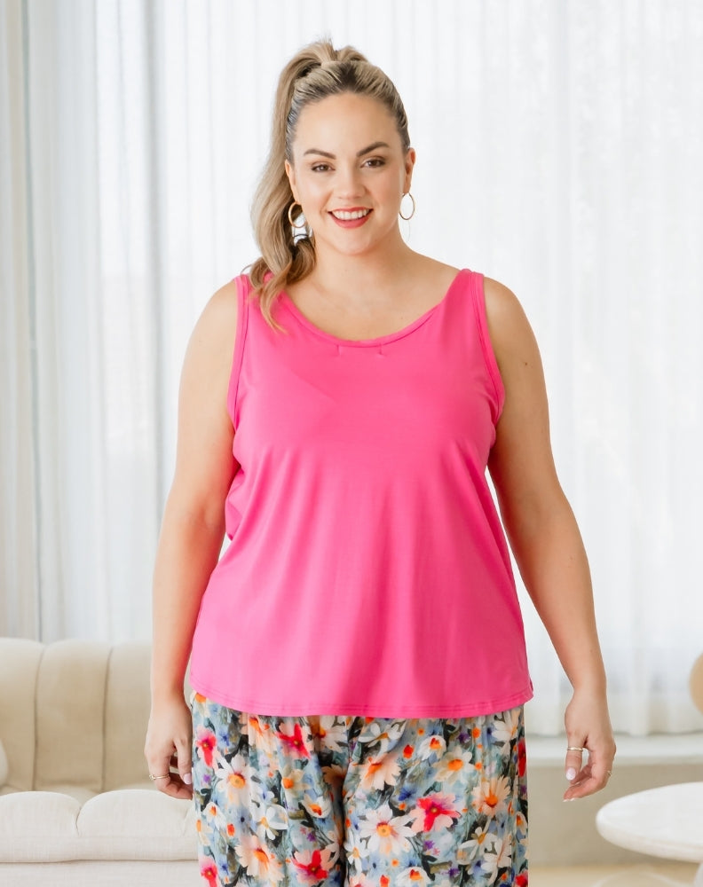 Woman wearing a bright pink tank top and floral pants indoors.