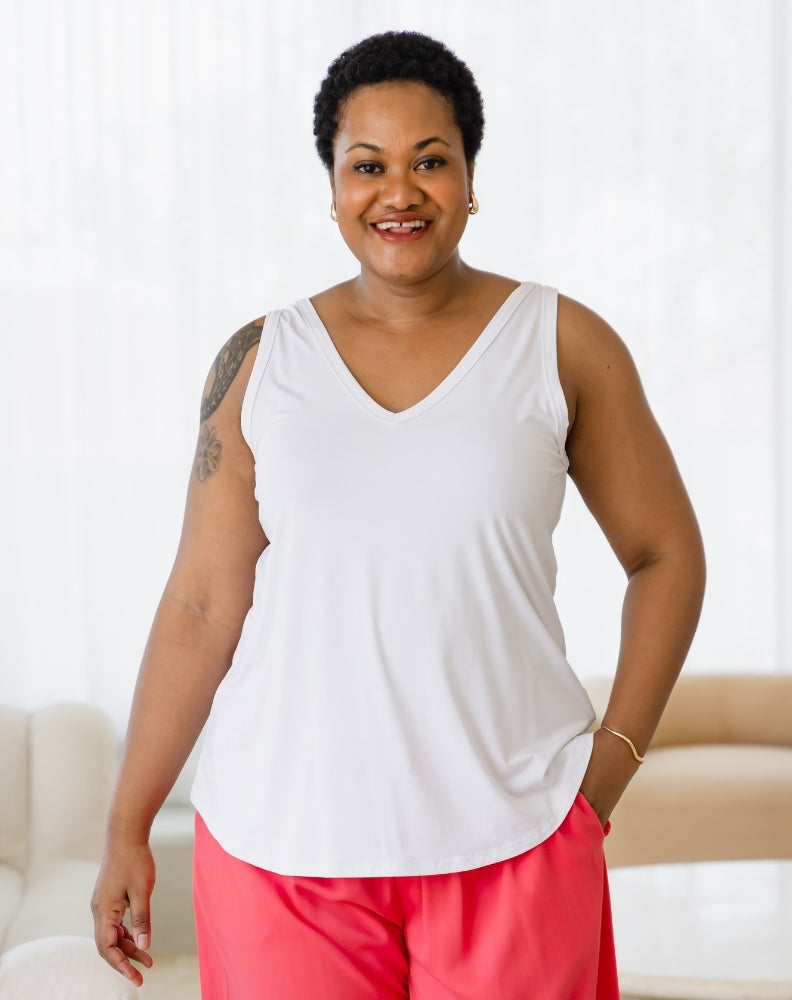 Woman wearing a white tank top and pink pants against a white background