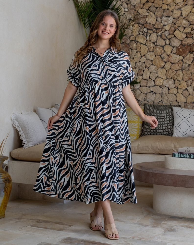 Woman in a zebra print dress standing in a living room with stone wall and sofa.