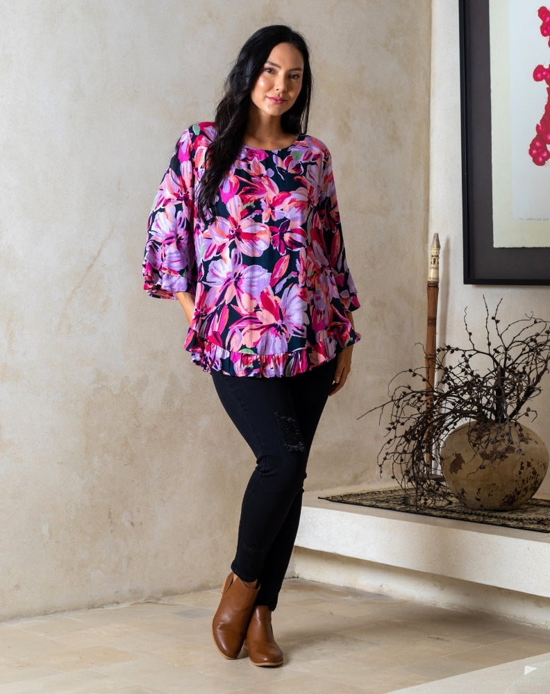 Woman wearing a colorful floral blouse and black pants standing indoors.