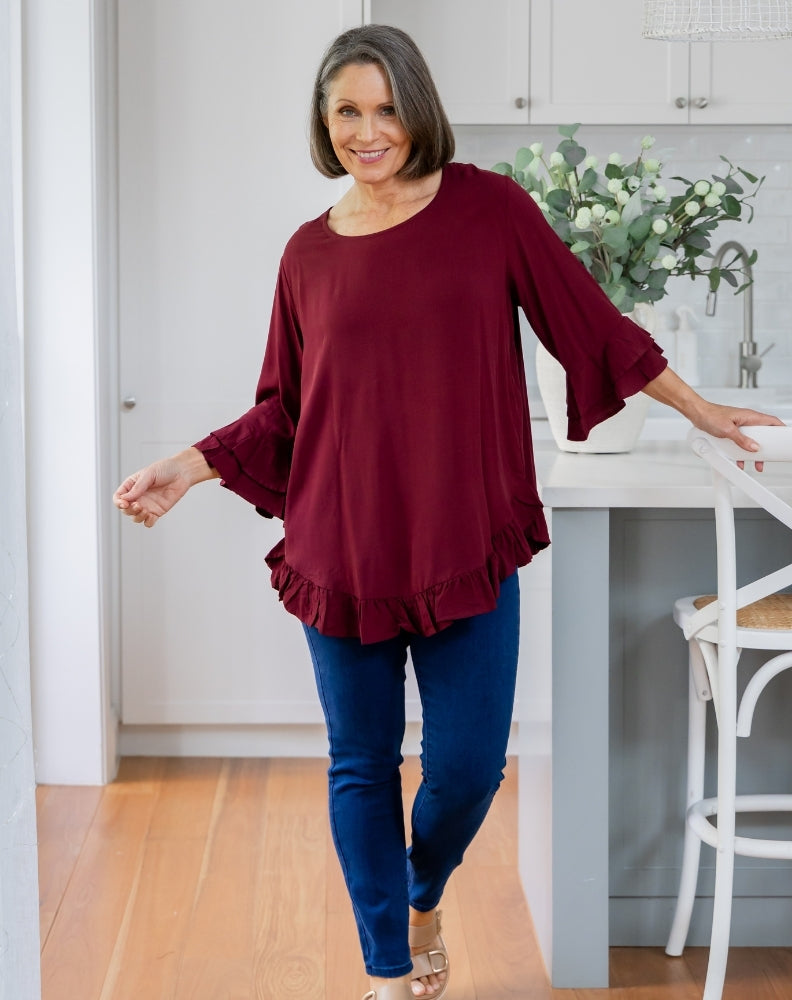 Woman wearing a burgundy top and blue jeans in a kitchen.