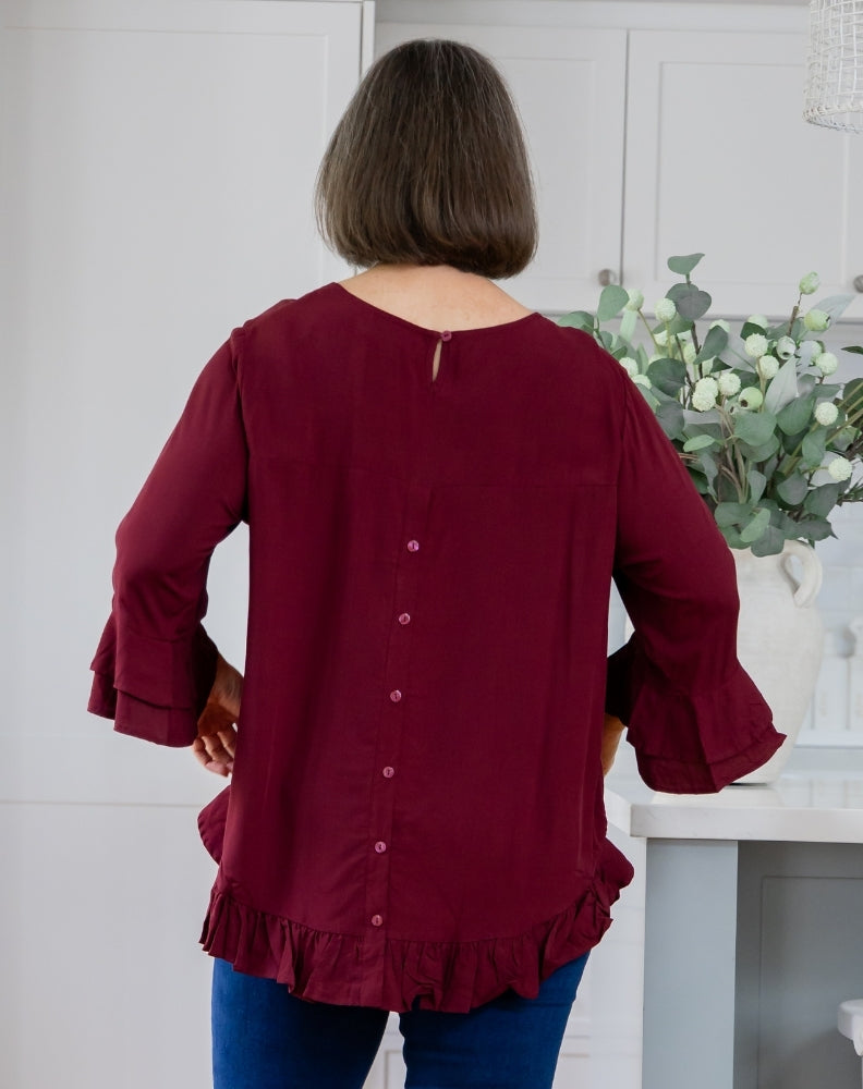 Person wearing a burgundy blouse with ruffled details in a kitchen setting