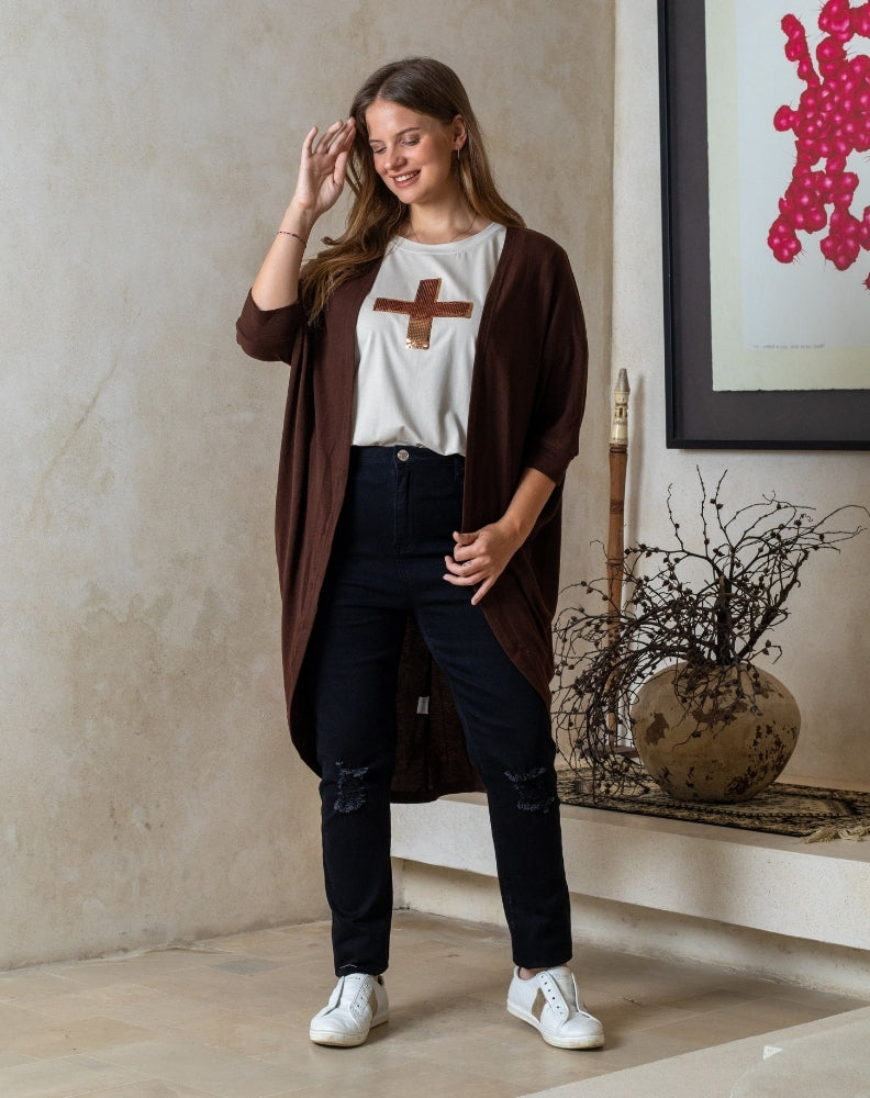 Woman wearing a brown cardigan, white shirt with a brown design, black pants, and white sneakers in an indoor setting.