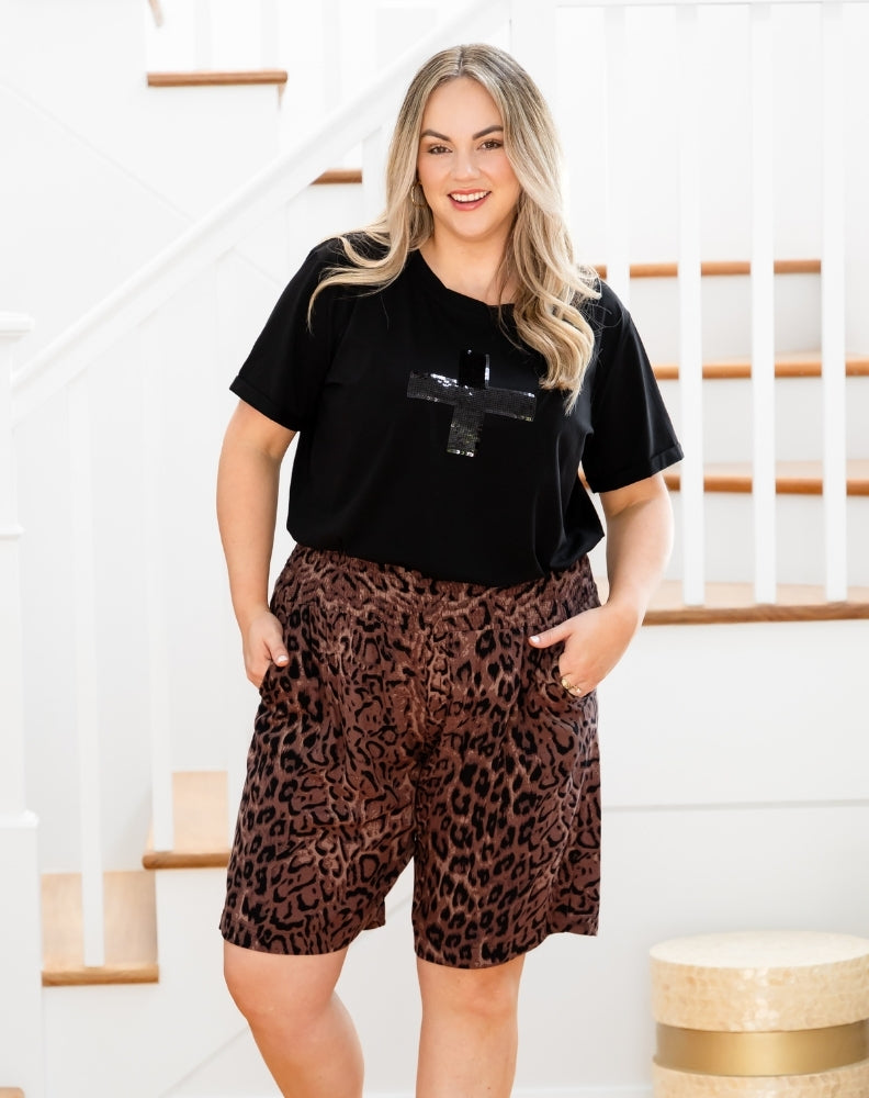 Woman wearing a black t-shirt and leopard print shorts standing indoors.