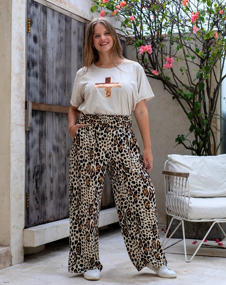 Woman wearing a white t-shirt with a graphic design and leopard print pants standing outdoors.