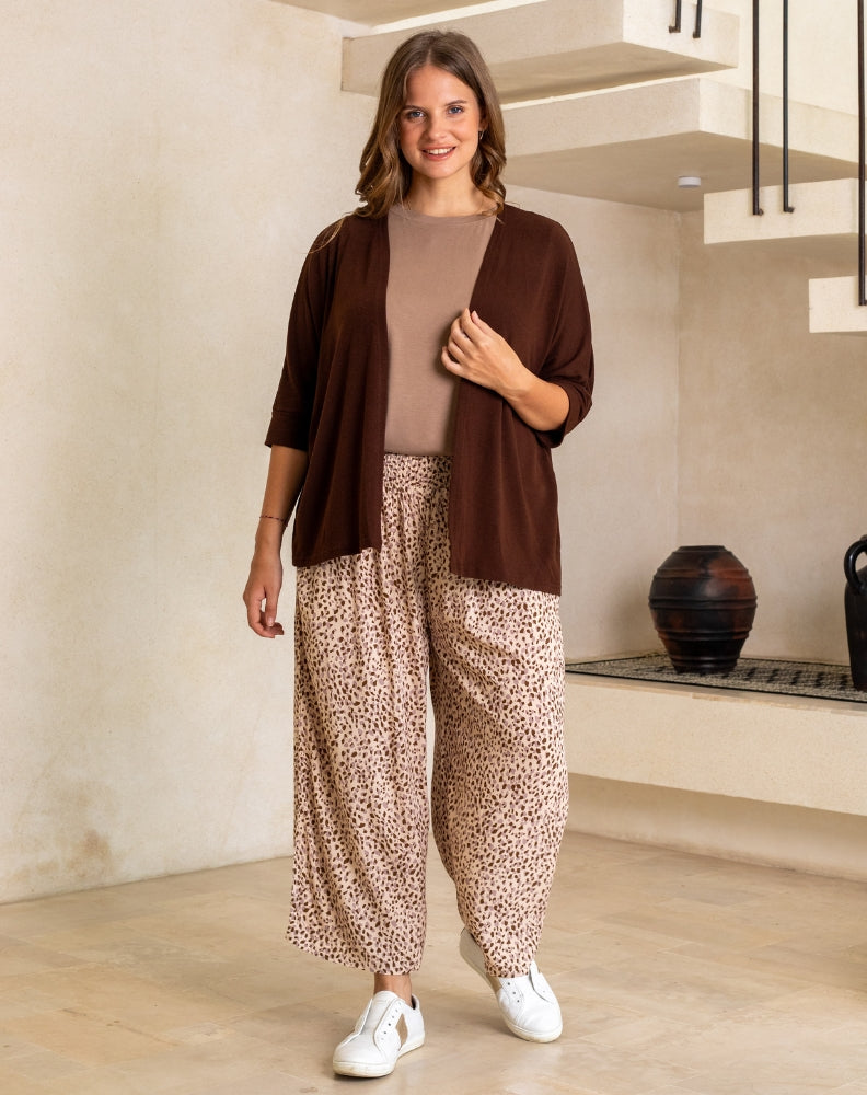 Woman wearing a brown cardigan, beige top, and patterned pants in a modern interior setting.