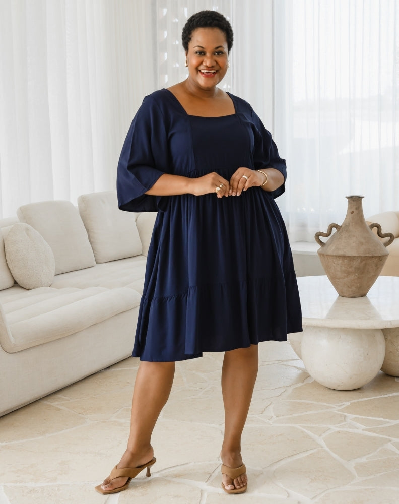 Woman in a navy blue dress standing in a living room.