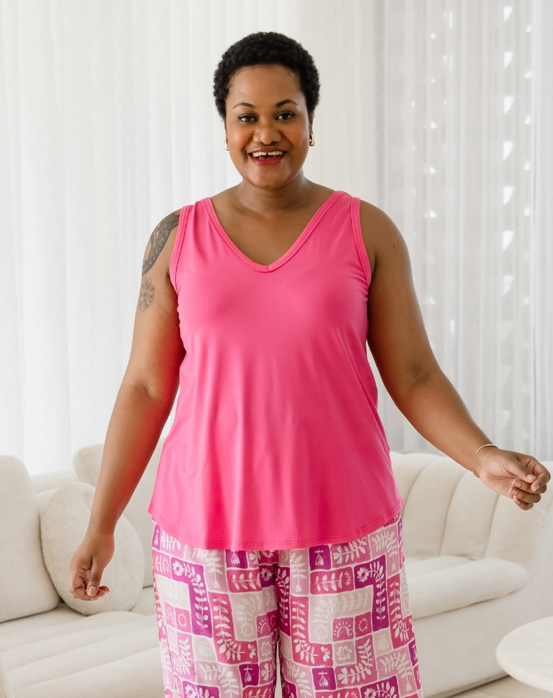 Woman wearing a pink tank top and patterned pants standing in a living room.