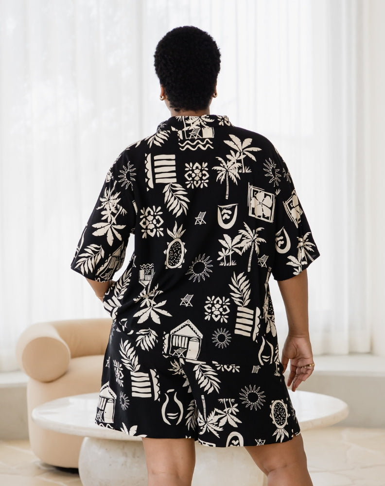 Person wearing a black shirt with white patterns in a room with white curtains and a beige chair.