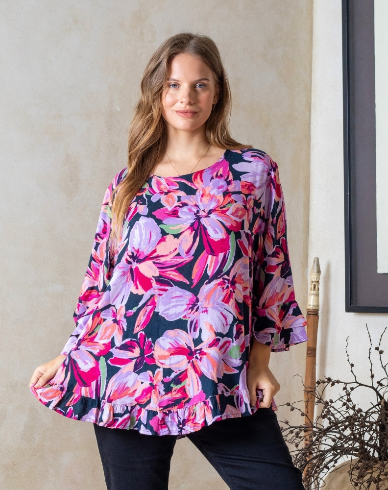 Woman wearing a colorful floral blouse against a neutral wall.