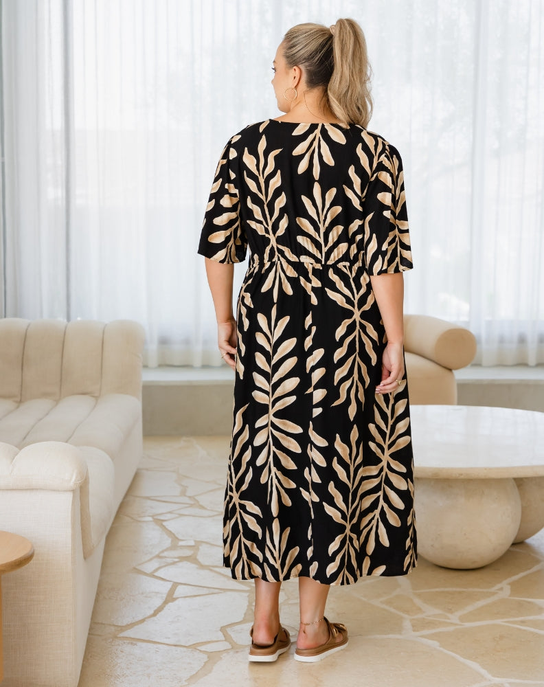 Woman wearing a black dress with beige leaf pattern in a modern living room.