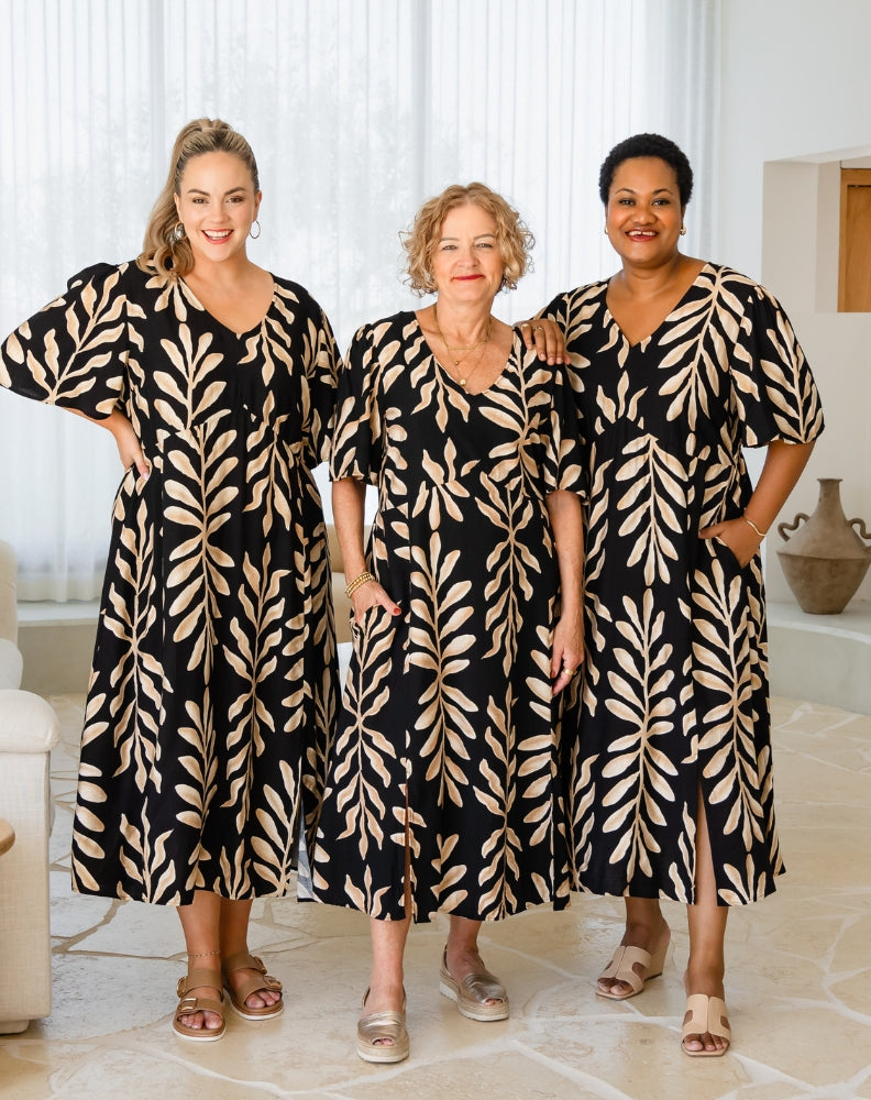 Three women wearing matching black and beige patterned dresses in a bright room.