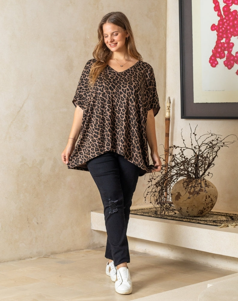 Woman wearing a leopard print top and black pants in a room with a decorative plant and abstract art.