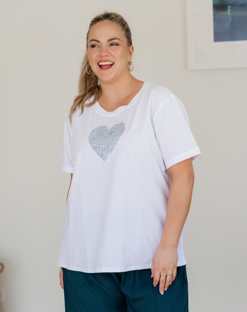Woman wearing a white t-shirt with a heart design, standing indoors.