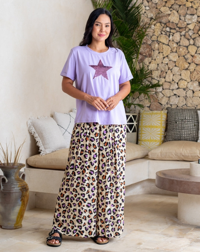 Woman wearing a purple t-shirt with a star design and leopard print pants in a living room setting.