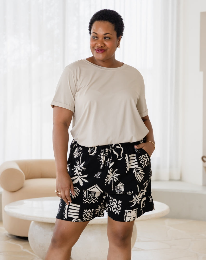 Woman wearing a beige top and black patterned shorts in a bright room.