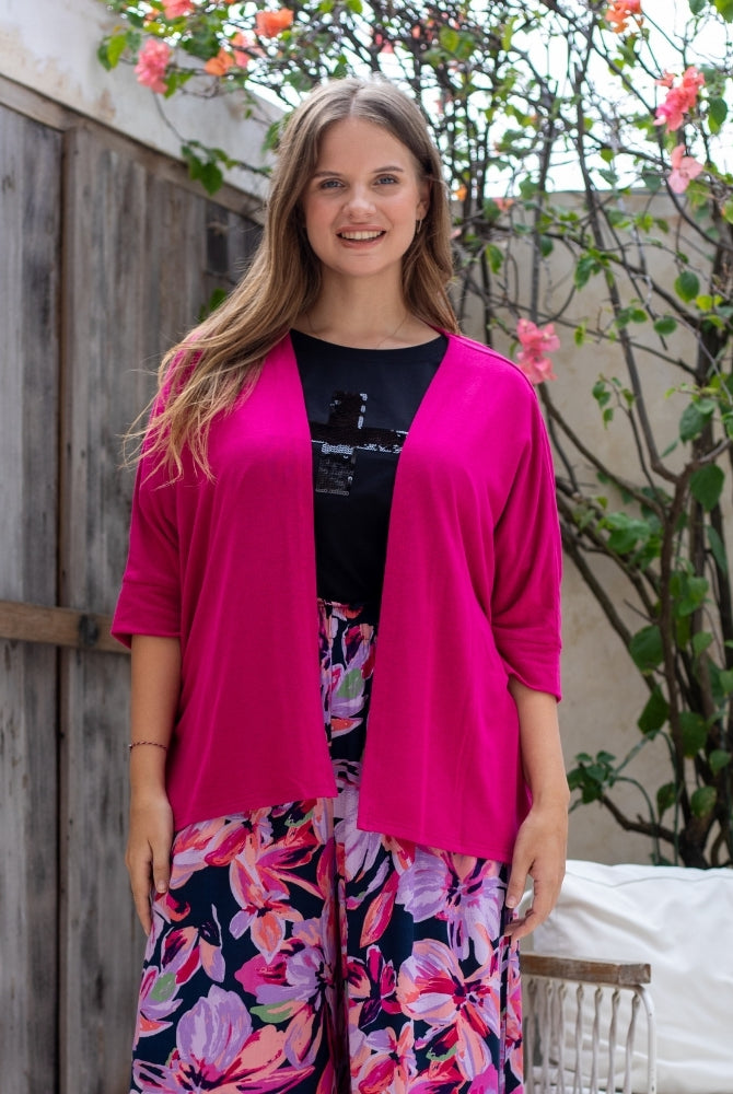 Woman wearing a bright pink cardigan over a black top with floral pants, standing outdoors.