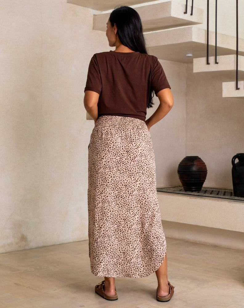 Woman in a brown top and patterned skirt standing in a room with a staircase.
