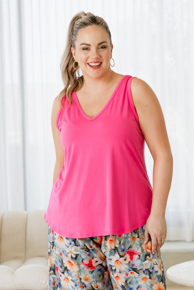 Woman wearing a bright pink tank top and floral pants indoors.