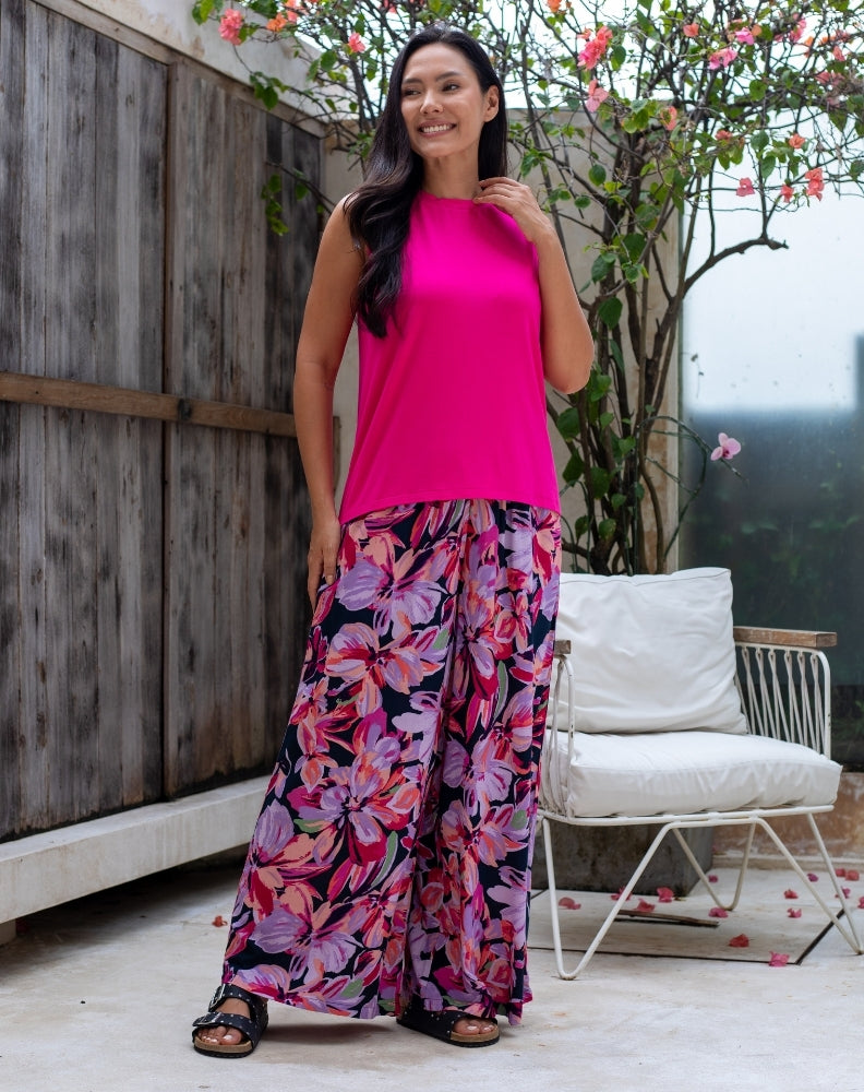 Woman wearing a bright pink top and floral pants standing outdoors.