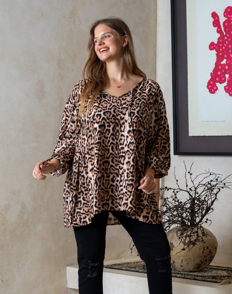 Woman wearing a leopard print top standing in a room with a decorative plant and abstract art.