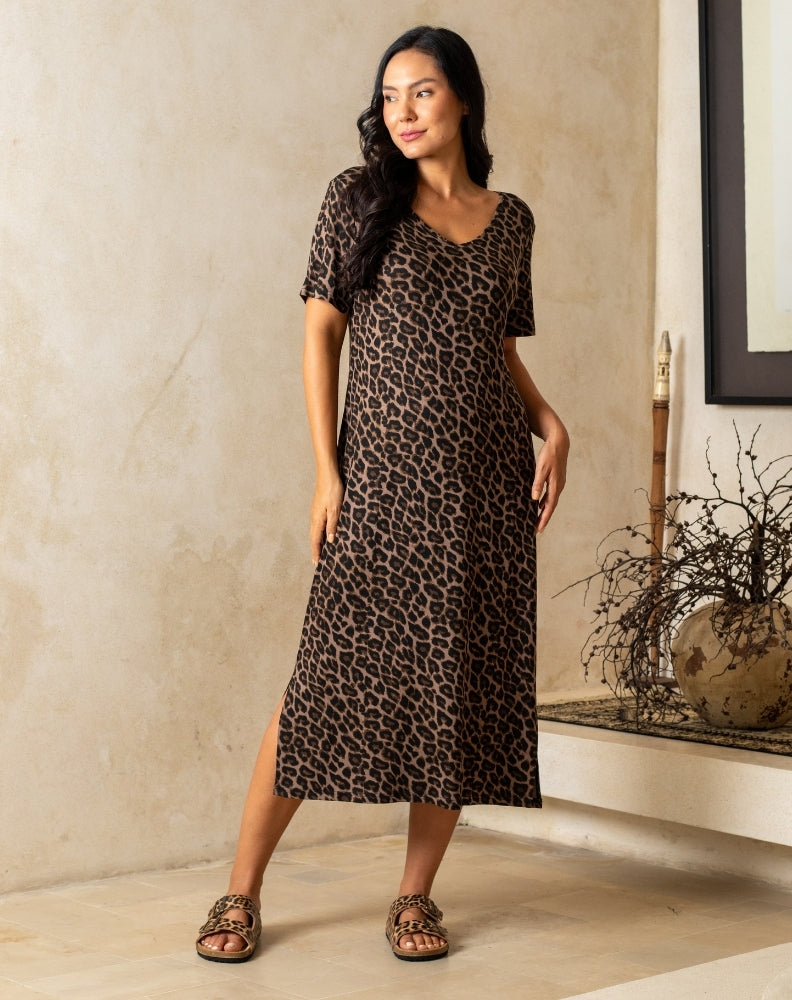 Woman wearing a leopard print dress standing in a room with a neutral wall and decorative elements.
