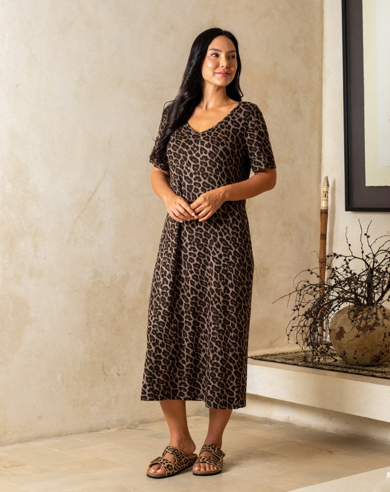 Woman wearing a leopard print dress standing in a room with a neutral wall and decorative elements.