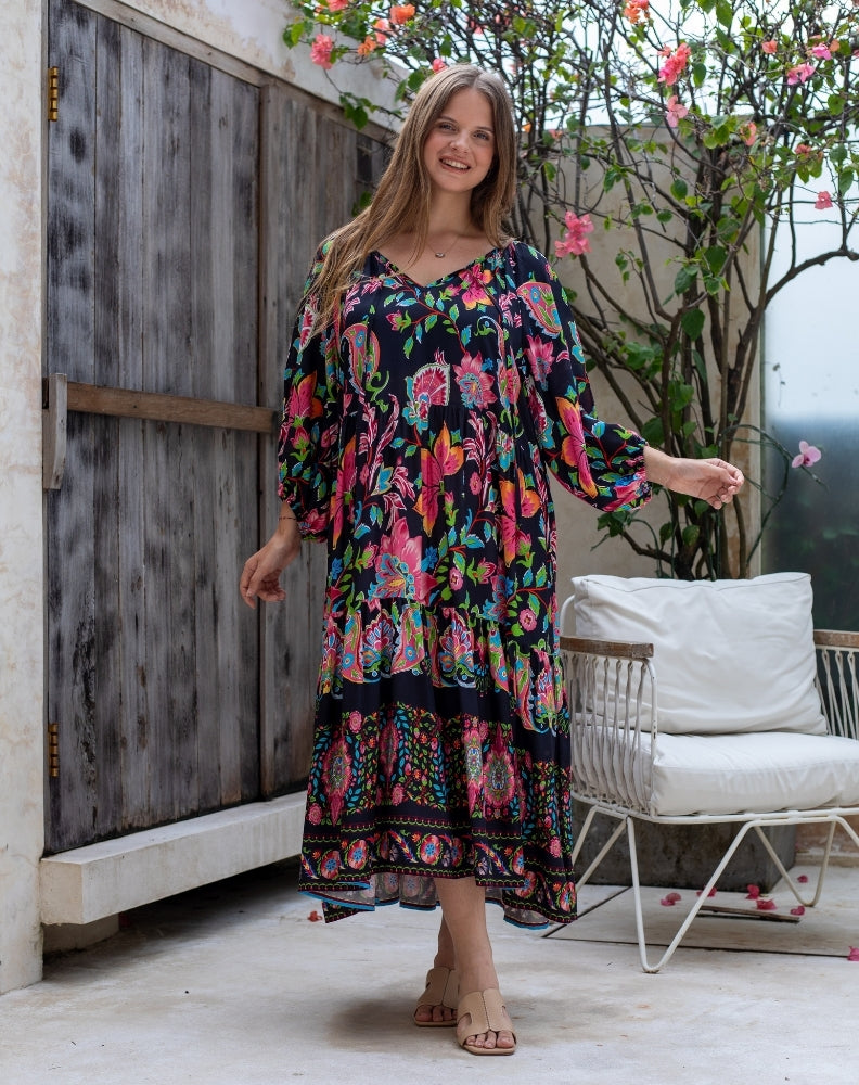 Woman in a colorful dress standing outdoors next to a chair and plant