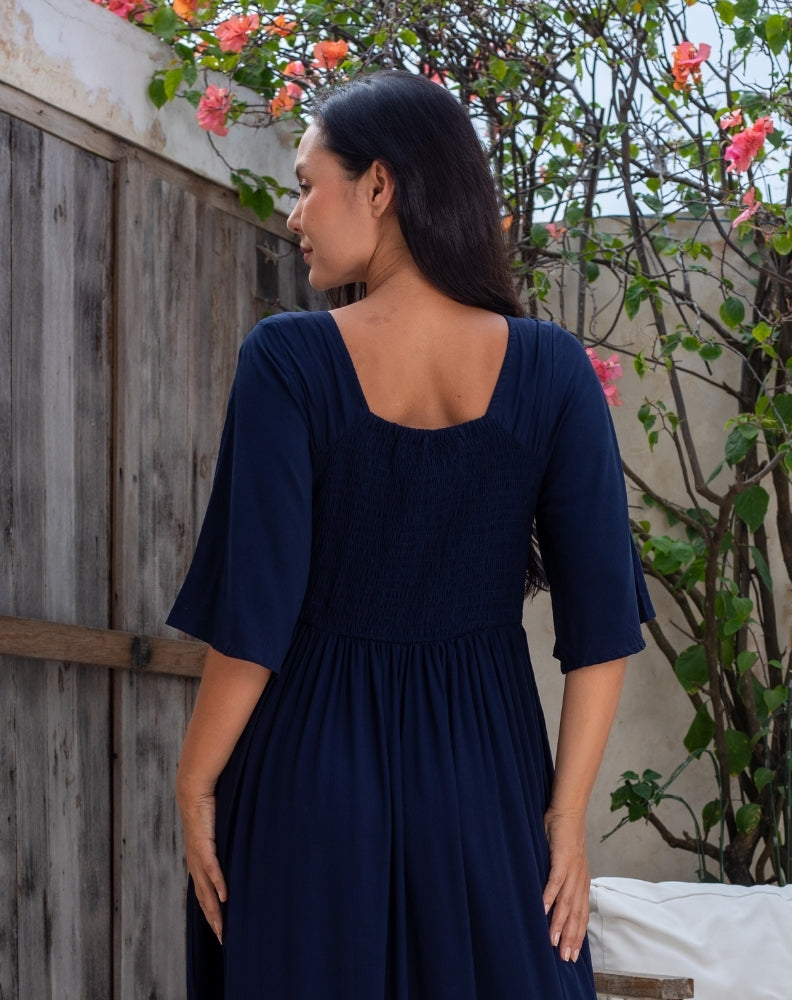 Woman wearing a navy blue dress standing outdoors with greenery in the background