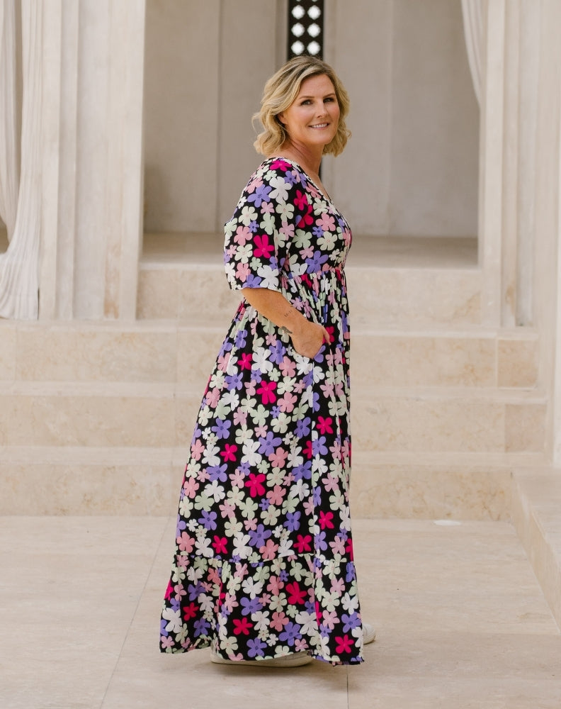 A woman modeling a long-sleeve maxi dress with a colorful floral print, standing in front of a stone staircase.