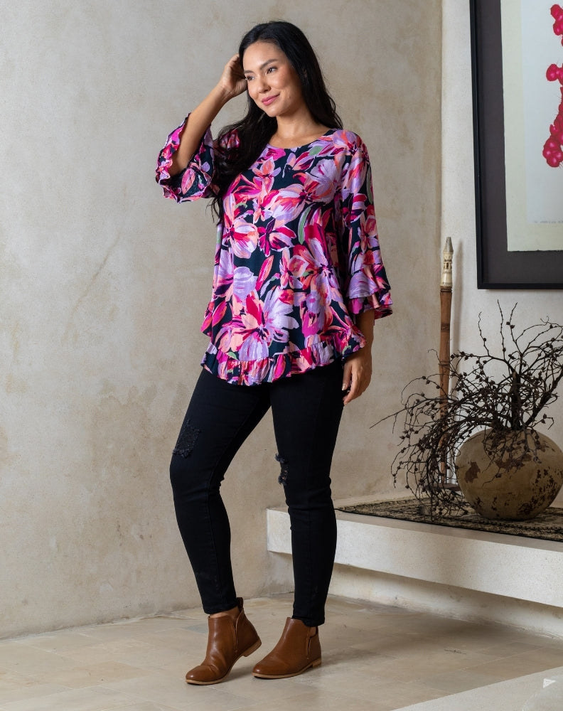 Woman wearing a colorful floral blouse and black pants indoors.