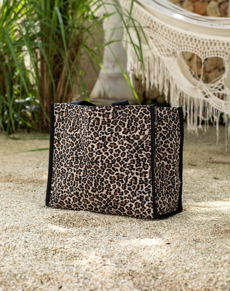 Leopard print bag on a sandy surface with plants and a chair in the background