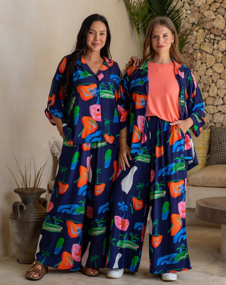 Two women wearing colorful outfits with a tropical pattern in a casual setting.