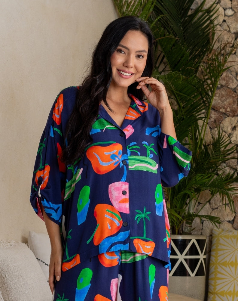 Woman wearing a colorful patterned dress standing indoors with plants in the background