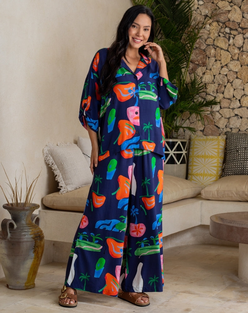 Woman wearing a colorful dress with a pattern of animals and plants in a living room setting.