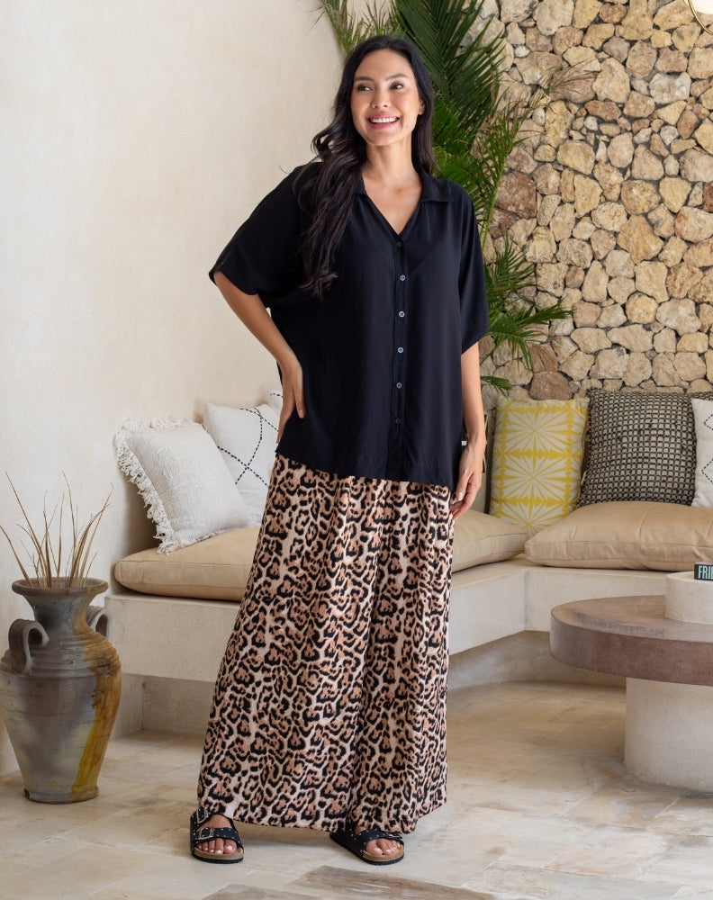 Woman wearing a black shirt and leopard print pants standing in a modern living room.