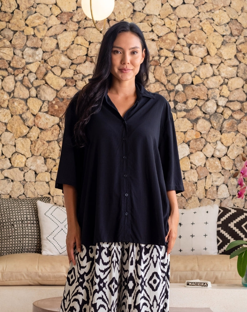 Woman wearing a black shirt and patterned pants standing in front of a stone wall.
