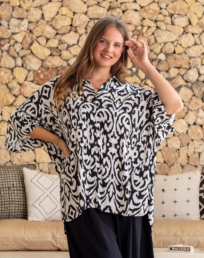 Woman wearing a black and white patterned blouse against a stone wall.