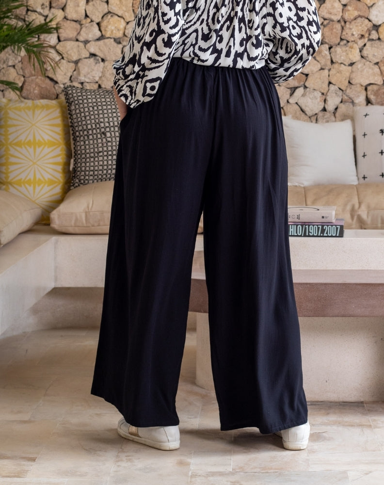 Person wearing black wide-leg pants and a patterned top in a living room setting.