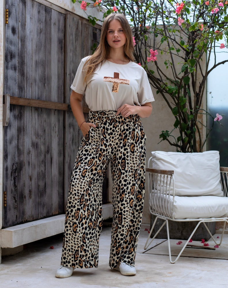 Woman wearing a white t-shirt with a graphic design and leopard print pants in an outdoor setting.