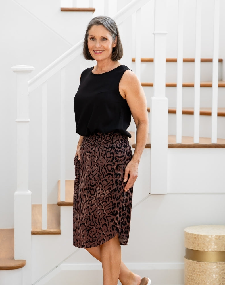 Woman wearing a black sleeveless top and leopard print skirt standing in a home setting.