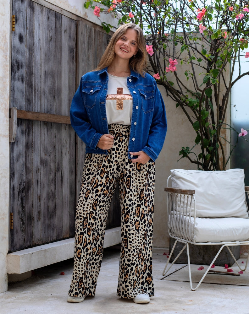 Woman wearing a blue denim jacket, white t-shirt, and leopard print pants standing in an outdoor setting.