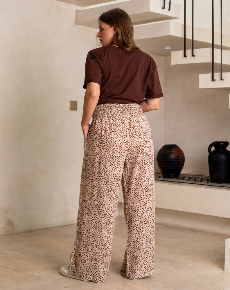 Woman wearing a brown top and leopard print pants in a room with a staircase.